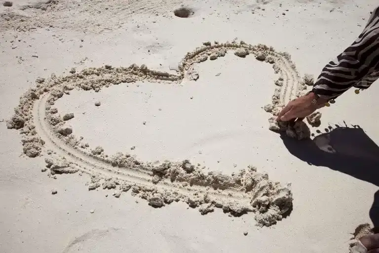 Hand zeichnet ein Herz in den Sand am Strand. Bewertungen Malediven: Romantische Geste im Paradies.
