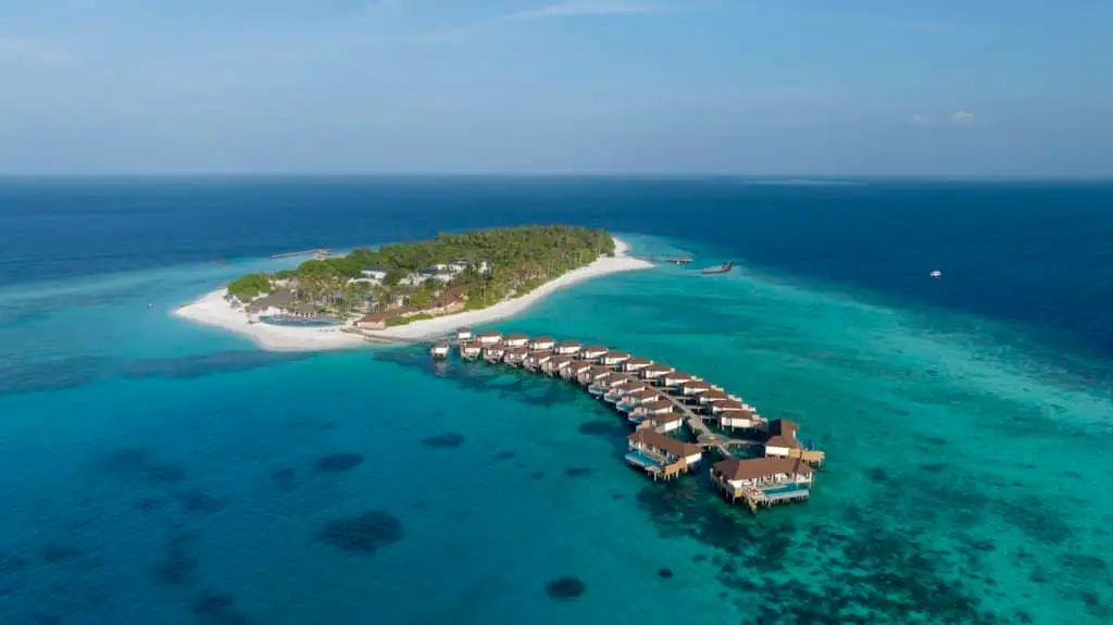 Luftaufnahme eines luxuriösen Avani+ Resorts auf einer tropischen Insel mit türkisfarbenem Wasser und Overwater-Bungalows.