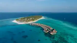 Luftaufnahme eines luxuriösen Avani+ Resorts auf einer tropischen Insel mit türkisfarbenem Wasser und Overwater-Bungalows.