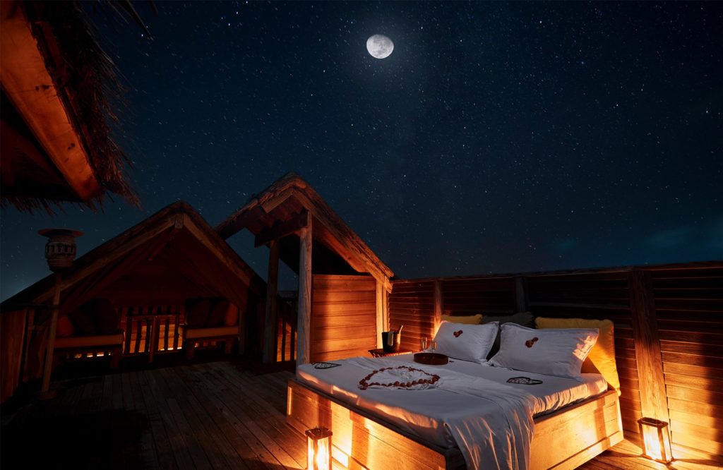 Romantisches Bett unter dem Sternenhimmel im Gili Lankanfushi Resort. Kerzenlicht, Mond und Sterne schaffen eine idyllische Atmosphäre. Luxusurlaub auf den Malediven.
