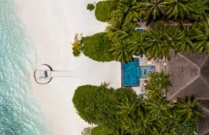 Luftaufnahme von Huvafen Fushi: Türkisblaues Wasser, weißer Sandstrand, üppige grüne Vegetation und ein luxuriöses Resort mit Pool. Ein Paradies!
