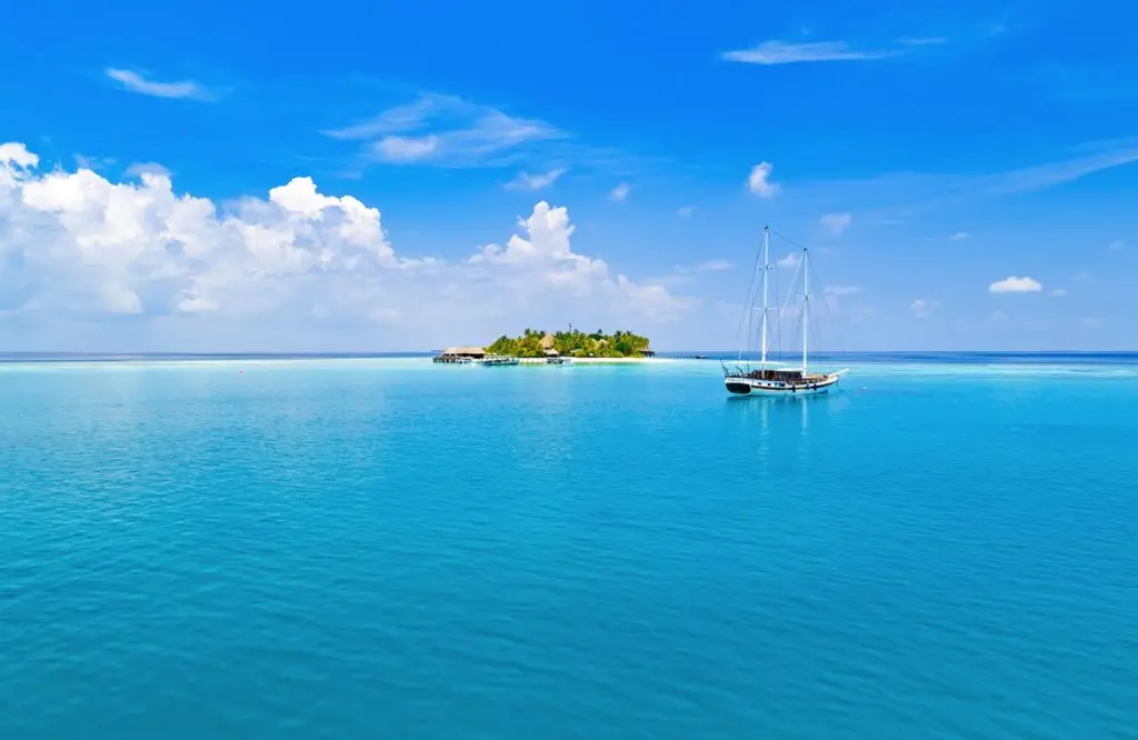 Segelboot vor Mirihi Island, türkisfarbenes Wasser und strahlend blauer Himmel mit Wolken. Luxuriöses Paradies bei V Villas Mirihi.