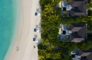 Luftaufnahme von Kuredhivaru: Türkisfarbenes Wasser trifft auf weißen Sandstrand, gesäumt von Palmen und luxuriösen Villen mit Pools.