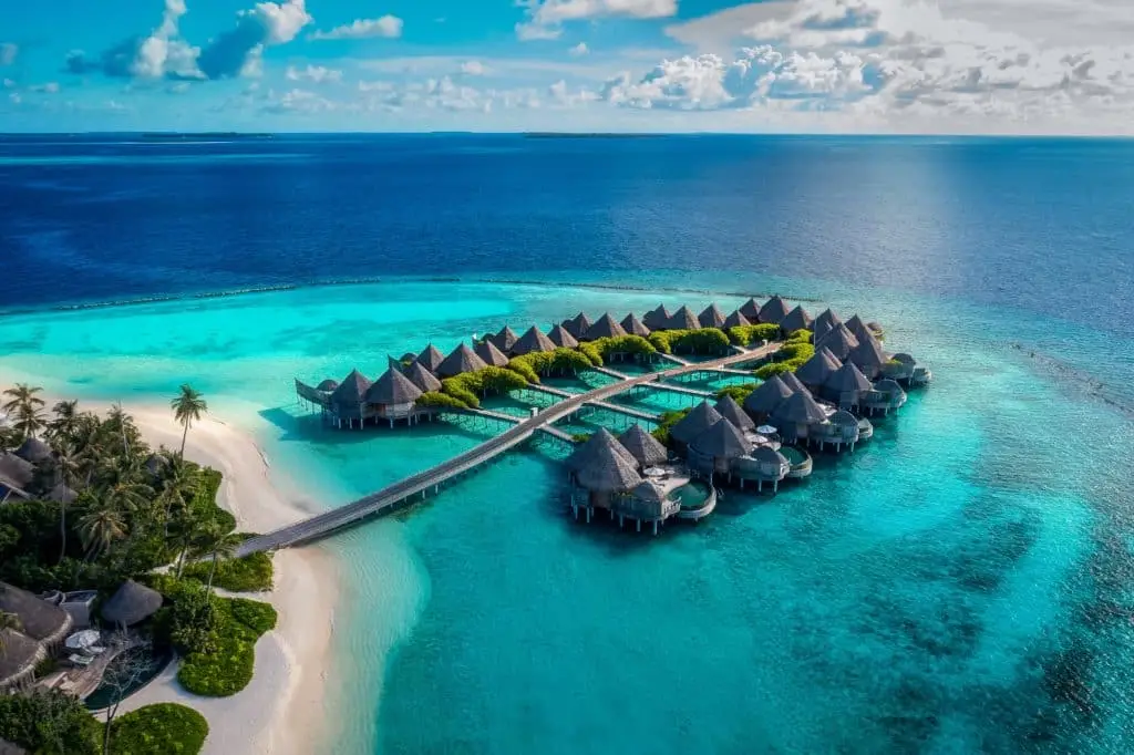Luxuriöses Wasserbungalow-Resort im The Nautilus Stil auf einer tropischen Malediveninsel mit türkisfarbenem Wasser und weißem Sandstrand unter blauem Himmel.