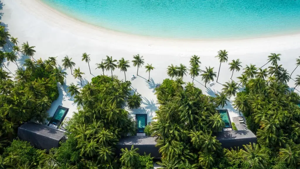 Luftaufnahme vom One & Only Reethi Rah: Türkisblaues Wasser, weißer Sandstrand, Palmen und luxuriöse Villen mit Pools im üppigen Grün.
