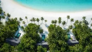 Luftaufnahme vom One & Only Reethi Rah: Türkisblaues Wasser, weißer Sandstrand, Palmen und luxuriöse Villen mit Pools im üppigen Grün.
