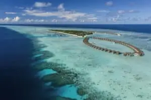 Luftaufnahme eines luxuriösen Pullman Resorts auf einer tropischen Insel mit Überwasserbungalows und türkisfarbenem Wasser.
