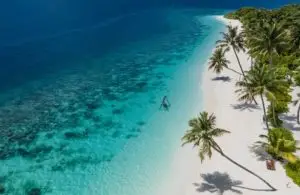 Luftaufnahme von Reethi Faru: Türkisblaues Wasser, weißer Sandstrand mit Palmen und einer Schaukel im Meer.