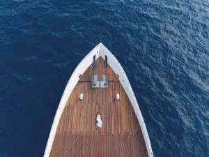 Draufsicht auf eine Frau im weißen Kleid, die sich auf dem Holzdeck einer Yacht entspannt. Tiefblaues Meer umgibt die Scubaspa. Luxuriöser Urlaub auf See.