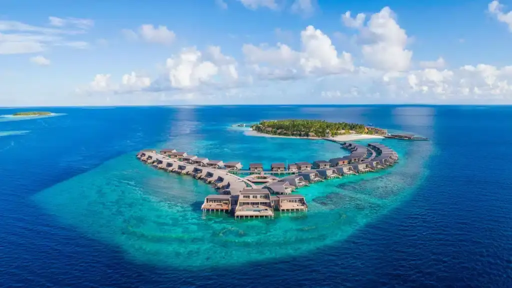 Luftaufnahme des luxuriösen St. Regis Vommuli Resorts auf einer tropischen Insel mit türkisfarbenem Wasser und strahlend blauem Himmel.