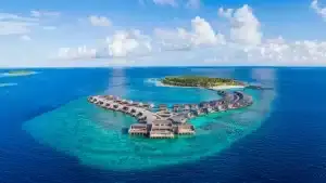 Luftaufnahme des luxuriösen St. Regis Vommuli Resorts auf einer tropischen Insel mit türkisfarbenem Wasser und strahlend blauem Himmel.