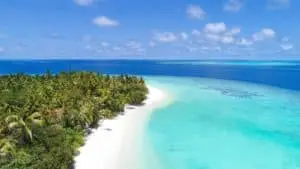 Luftaufnahme von Vakkaru, einer tropischen Insel mit üppiger Vegetation, weißem Sandstrand und türkisfarbenem Wasser unter strahlend blauem Himmel.