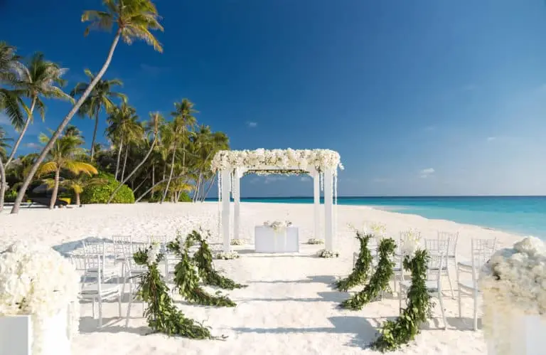 Romantische Hochzeit auf den Malediven: Weißer Baldachin, geschmückte Stühle am Strand unter Palmen. Türkisblaues Meer im Hintergrund. Heiraten auf den Malediven, ein Traum!