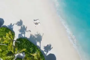 Luftaufnahme eines unberührten Strandes im Waldorf Astoria mit türkisfarbenem Wasser, weißem Sand und zwei Liegestühlen unter Palmen. Perfekt für einen luxuriösen Urlaub.