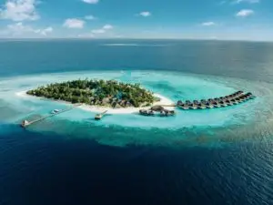 Luftaufnahme einer tropischen Insel mit Luxus-Wasserbungalows in den Malediven. Türkisfarbenes Wasser umgibt die Insel, die ein Paradies für Nova-Reisen darstellt.