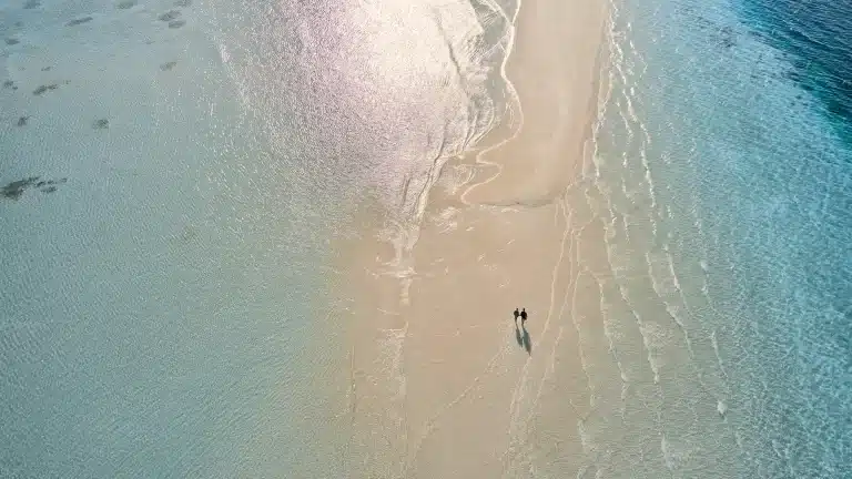 Luftaufnahme: Zwei Personen spazieren auf einer hellen Sandbank, umgeben von türkisfarbenem Wasser. Ein idyllischer Ort für Wiederholungsgäste.