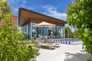 Luxuriöse Strandvilla mit Pool auf den Malediven. Moderne Architektur mit Glasfront, Liegestühlen und Sonnenschirm. Paradiesisches SO-Resort für Entspannung.