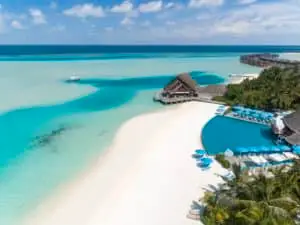Luftaufnahme vom Luxusresort Anantara Dhigu, Malediven: Türkisblaues Wasser, weisser Sandstrand, Pool und Wasserbungalows unter strahlend blauem Himmel.