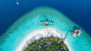 Luftaufnahme von Anantara Kihavah: Luxuriöse Wasserbungalows und Villen auf einer tropischen Insel mit türkisfarbenem Wasser und weißem Sandstrand.