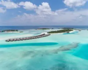 Luftaufnahme von Naladhu, Malediven: Türkisblaues Wasser umgibt luxuriöse Wasserbungalows, die sich an einem strahlend sonnigen Tag über eine Sandbank erstrecken.