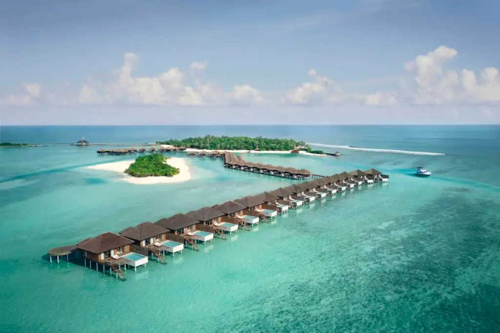 Luftaufnahme des Anantara Veli Resorts auf den Malediven: Luxuriöse Wasserbungalows mit privaten Pools über türkisfarbenem Wasser, verbunden mit einer grünen Insel. Ein Paradies für einen unvergesslichen Urlaub.