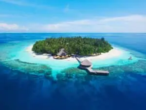 Luftaufnahme von Dhawa Ihuru, einer tropischen Insel mit weißem Sandstrand, üppiger Vegetation und einem Steg mit strohgedecktem Pavillon im türkisfarbenen Wasser.