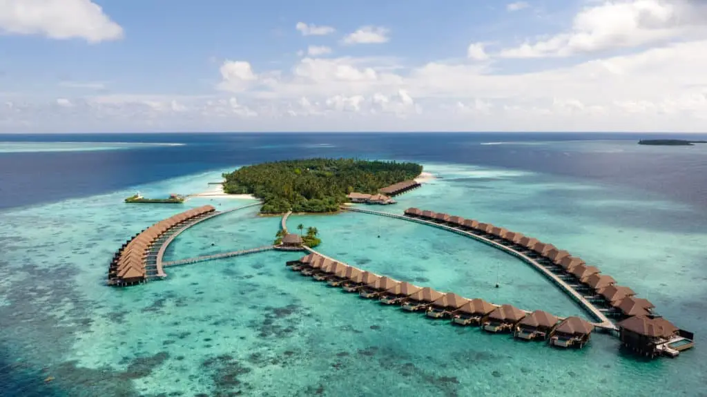 Luftaufnahme von Ayada Malediven, mit luxuriösen Wasserbungalows, die sich halbkreisförmig um eine tropische Insel mit türkisfarbenem Wasser schmiegen. Ein Paradies für Entspannung.