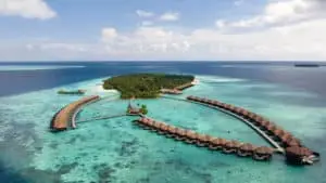 Luftaufnahme von Ayada Malediven, mit luxuriösen Wasserbungalows, die sich halbkreisförmig um eine tropische Insel mit türkisfarbenem Wasser schmiegen. Ein Paradies für Entspannung.