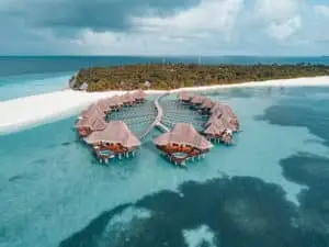 Luftaufnahme von Luxus-Wasserbungalows mit Strohdächern im Coco Palm Dhuni Kolhu Resort, Malediven. Türkisfarbenes Wasser umgibt die Anlage.