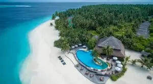 Luftaufnahme des Filitheyo Island Resort: Türkisblaues Wasser, weißer Sandstrand, üppige grüne Vegetation und ein einladender Pool mit Strohdach-Restaurant.