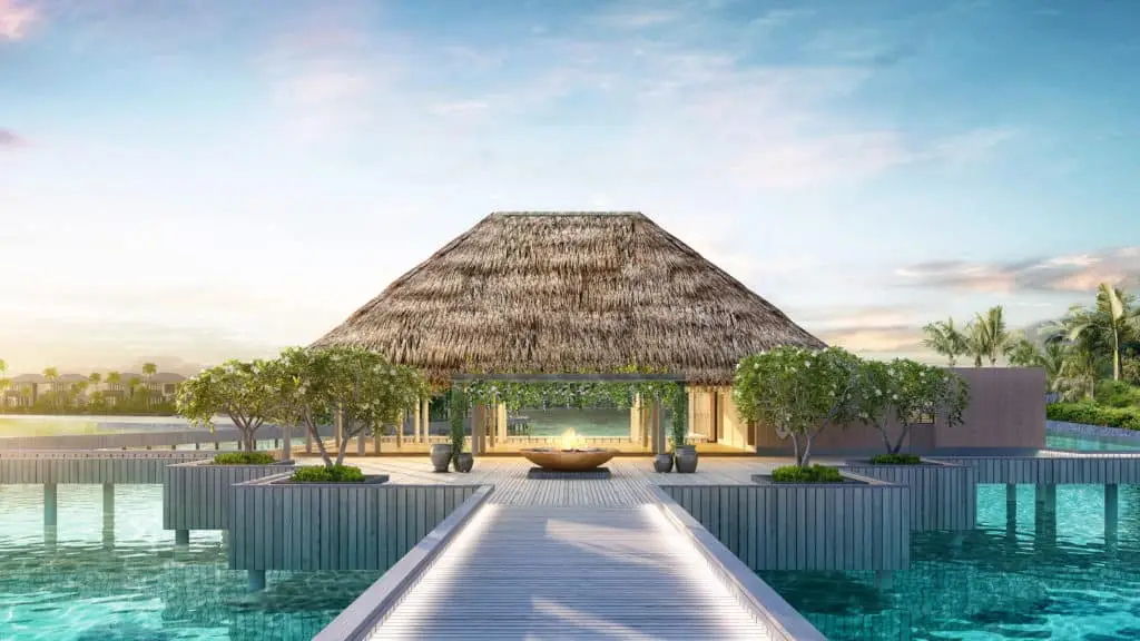 Luxuriöses InterContinental Maamunagau Resort: Strohgedecktes Gebäude auf Stelzen über türkisfarbenem Wasser, verbunden durch einen Holzsteg. Tropische Bäume und strahlend blauer Himmel.