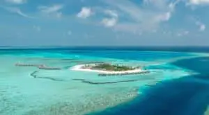 Luftaufnahme von "You & Me by Cocoon", einem luxuriösen Inselresort auf den Malediven. Türkisfarbenes Wasser umgibt die Insel mit Wasserbungalows und üppiger Vegetation.