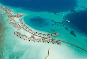 Luftaufnahme von Constance Halaveli: Luxuriöse Wasserbungalows mit Strohdächern auf türkisfarbenem Wasser, verbunden durch Stege. Ein Paradies in den Malediven.