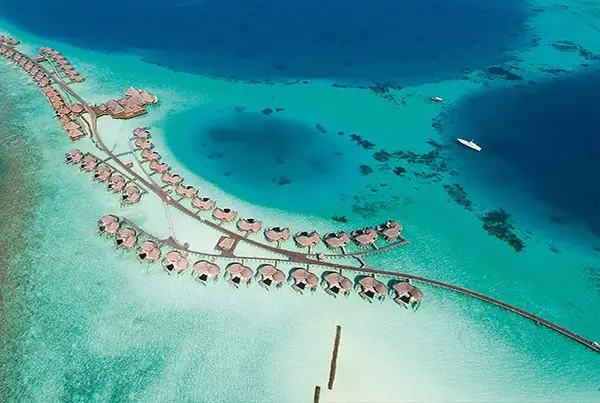 Luftaufnahme von Constance Halaveli: Luxuriöse Wasserbungalows mit Strohdächern auf türkisfarbenem Wasser, verbunden durch Stege. Ein Paradies in den Malediven.