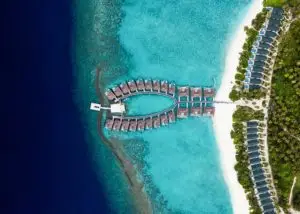Luftaufnahme von Furaveri Island: Luxuriöse Wasserbungalows in Fischform über türkisfarbenem Wasser, flankiert von einem weißen Sandstrand und üppigem Grün.