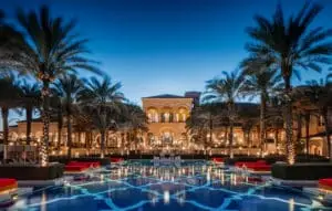 Exklusives Strandhotel Dubai: Das One & Only The Palm bei Nacht. Beleuchteter Pool spiegelt Palmen und die Fassade des Hotels wider, unter tiefblauem Himmel.