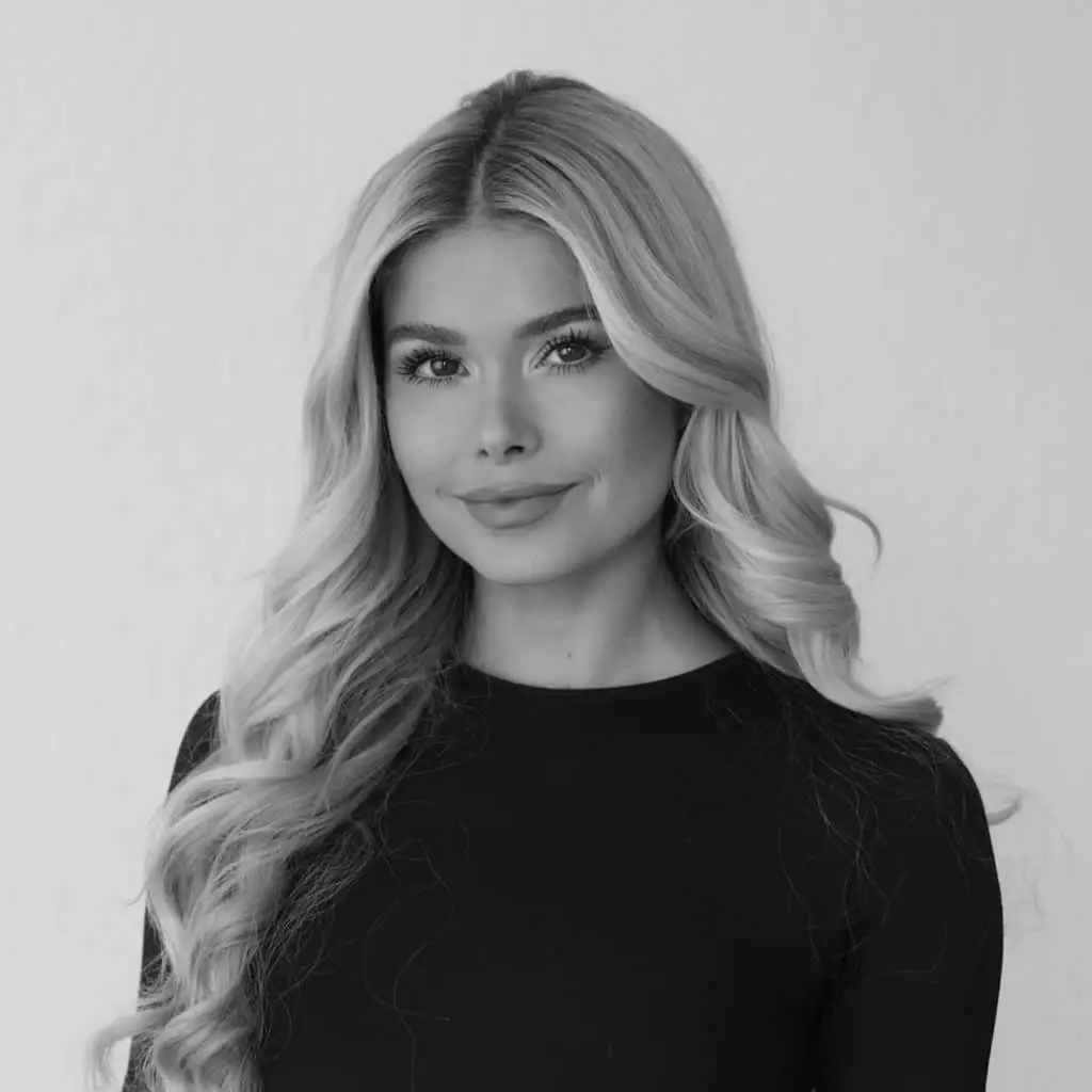 Blonde Frau mit welligem Haar und schwarzem Oberteil vor einem weißen Hintergrund. Ideal für die Buchung eines Malediven Urlaubs oder eines Malediven Hotels.