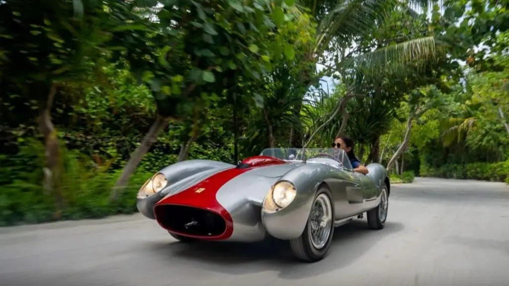 Ferrari Luxus auf den Malediven: Eine Frau fährt einen silbernen Ferrari vor dem Waldorf Astoria Ithaafushi, umgeben von tropischer Vegetation.
