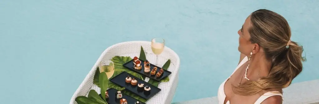 Frau mit Cocktail und Snacks am Pool auf den Malediven. Luxus All Inclusive Urlaub mit kulinarischen Genüssen und Entspannung pur.