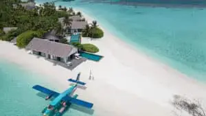 Wasserflugzeug am weißen Sandstrand von Four Seasons Private Island Voavah, Malediven. Türkisfarbenes Wasser und Luxusvillen mit Pools im Hintergrund.