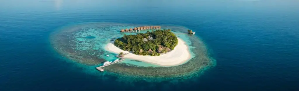 Luftaufnahme von Kandolhu Maldives: Eine tropische Insel mit weißen Sandstränden, üppiger Vegetation und luxuriösen Wasserbungalows im türkisfarbenen Ozean.