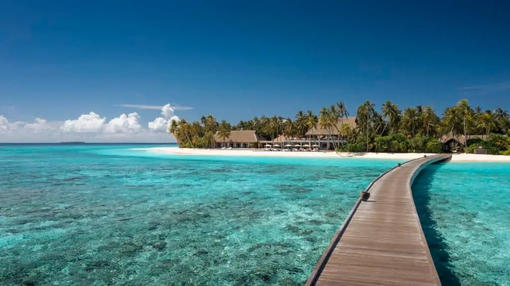 Holzsteg führt zu Velaa, einem luxuriösen Inselresort auf den Malediven. Türkisblaues Meer, weißer Sandstrand und Palmen unter strahlend blauem Himmel. Luxus und Meer vereint.