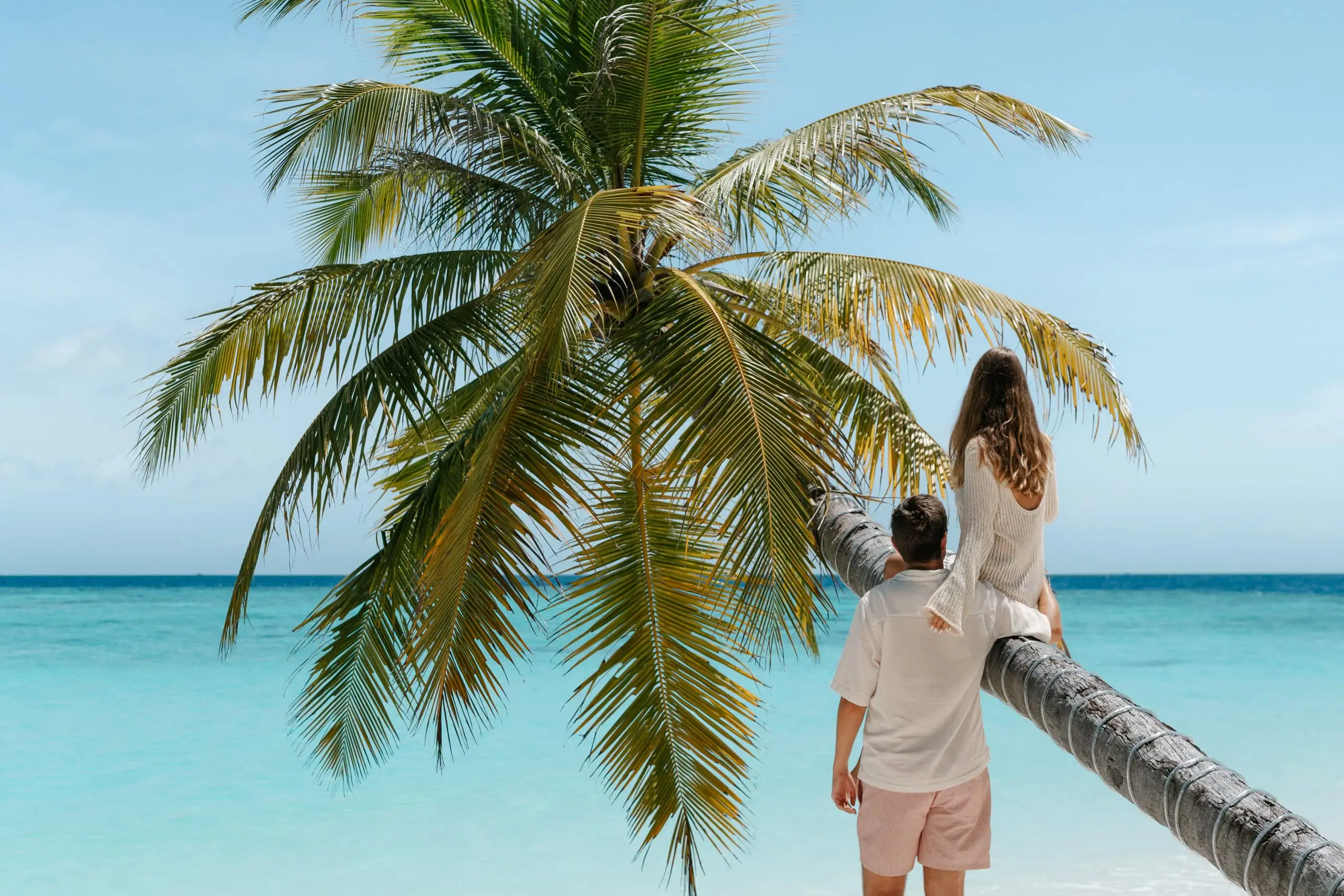 Ein Paar sitzt auf einer geneigten Palme am Strand mit türkisfarbenem Wasser. @culinary.jetsetters genießen die tropische Aussicht.