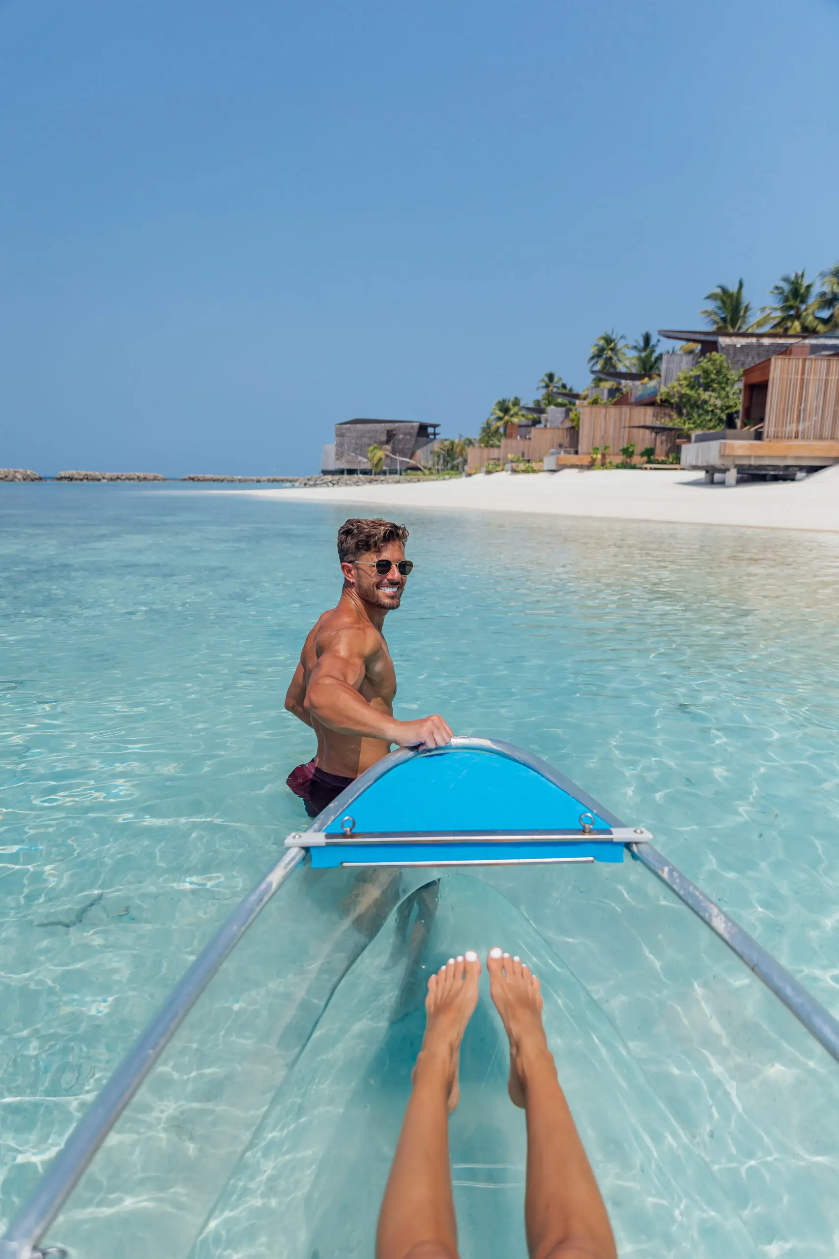 Mann zieht ein transparentes Kajak durch flaches, türkisfarbenes Wasser an einem tropischen Strand