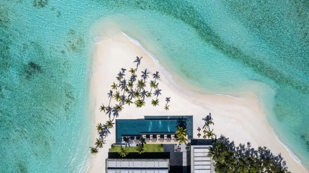 Luftaufnahme einer tropischen Insel mit weißem Sandstrand, Palmen und türkisfarbenem Wasser neben einer Anlage mit Pool auf den Malediven