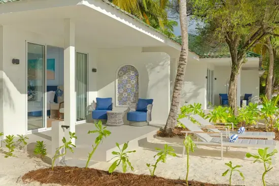 Terrasse eines Ferienhauses mit Liegestühlen, blauen Sesseln und tropischer Bepflanzung