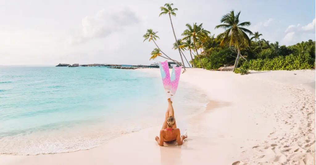 Frau mit Flossen liegt am weißen Sandstrand vor türkisfarbenem Meer und Palmen