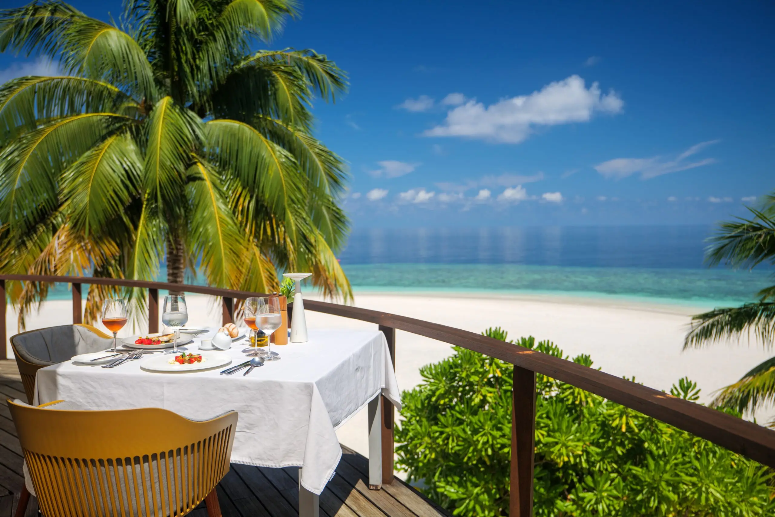 Romantisch gedeckter Tisch auf einer Terrasse mit Meerblick und Palmen am Strand